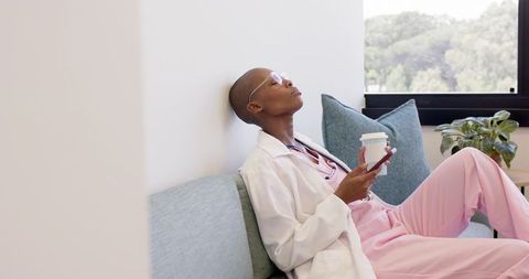 African healthcare professional relaxing on clinic bench holding coffee and phone