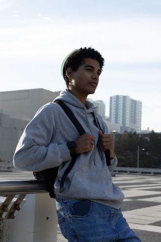 Contemplative african american teen leaning on overpass rail wearing hoodie and backpack