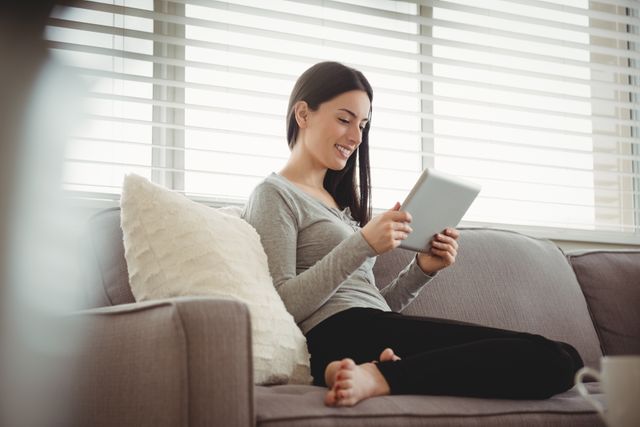 Smiling woman holding tablet while sitting on sofa at home