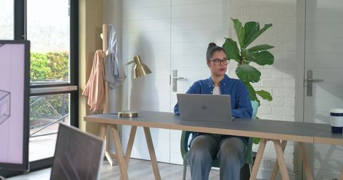 Young woman working on laptop at minimalist wooden trestle desk in bright home office