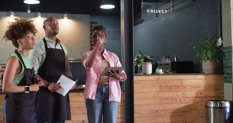 Cafe manager briefing barista team with tablet and papers at wooden counter