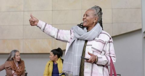 Senior African-American woman giving thumb-up while holding smartphone and waiting in lobby
