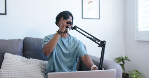 Recording podcast at home adjusting boom arm microphone with laptop on sofa