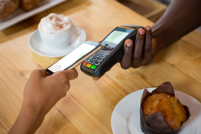 Customer making a contactless payment using a smartphone at a cafe. Barista holding a POS terminal. Ideal for illustrating modern payment methods, digital transactions, and convenience in coffee shops. Can be used in articles about technology in retail, mobile payment systems, and cashless transactions.