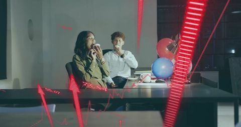 Coworkers celebrating with cupcakes and balloons at desk with financial charts overlay