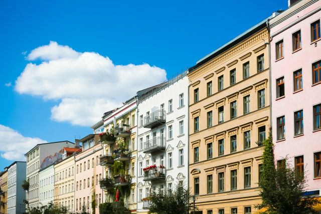 Colorful row of historic residential buildings with balconies and windows, set against a bright blue sky with fluffy white clouds. Perfect for articles or content about urban living, European architecture, and travel destinations. Can also be used for real estate websites and city planning presentations.