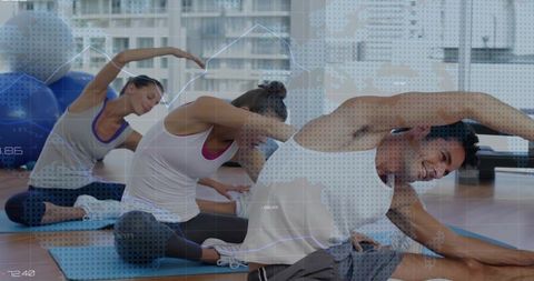 Group stretching doing seated side-bends on blue mats in urban studio with exercise balls
