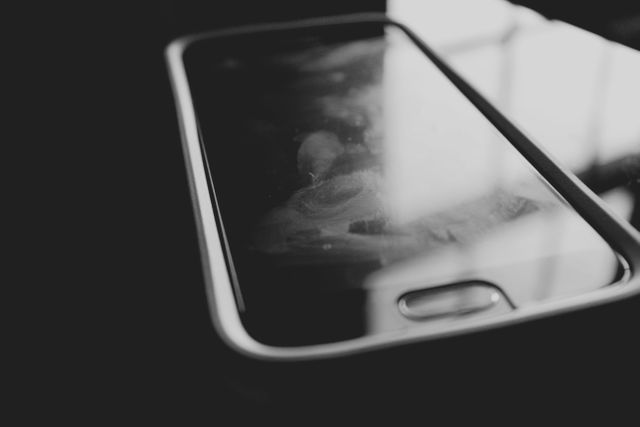 Close-up of a smartphone with visible fingerprints all over a dark screen. The black and white effect adds a dramatic tone and emphasizes the neglected and used nature of the device. Suitable for concepts related to technology usage, mobile phone hygiene, or showing the side effects of frequent device handling.
