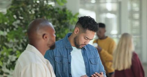 Diverse coworkers chatting in modern office lobby, african american man checking phone