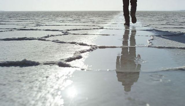 Walking on reflective salt flat leaving vertical reflection over geometric crust patterns