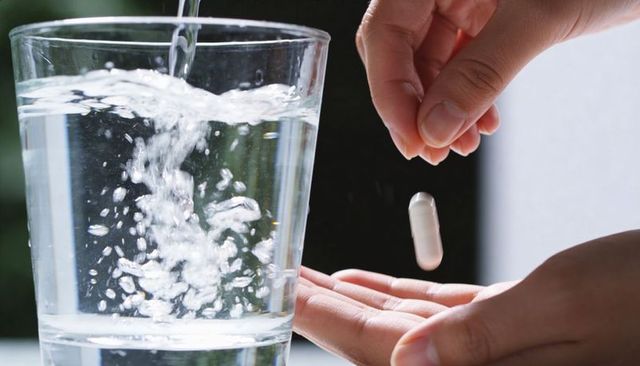 Hands dropping white capsule into glass of water with bubbling effervescence for medication routine