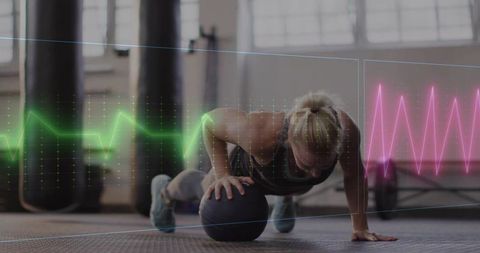 Woman performing medicine ball pushup with heartbeat waveform overlay in industrial gym