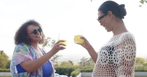 Friends toasting with yellow cocktails on sunny terrace overlooking city skyline