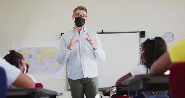 Teacher wearing protective face mask instructing students in classroom, emphasizing education amidst health safety protocols. Ideal for illustrating pandemic lifestyle, educational settings, health and safety measures, and teaching during COVID-19.