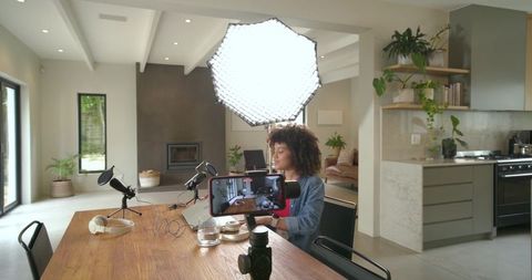 African american woman recording podcast at home with softbox lighting and smartphone