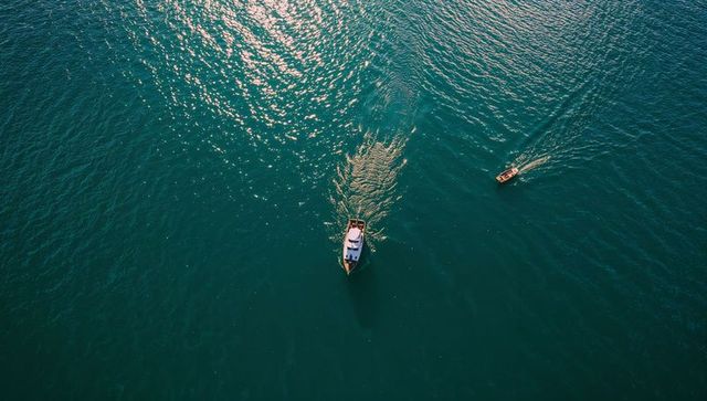 Aerial motorboat cutting through teal sea with glinting sunlight and nearby skiff