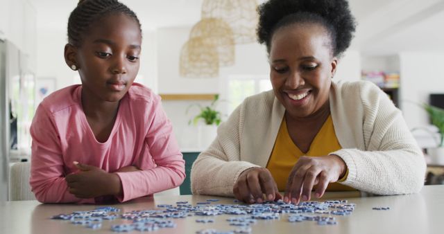 A mother and daughter are spending quality time solving a puzzle together at home. The mother is concentrating on placing the puzzle pieces while the daughter observes. This image represents family bonding, cooperation, and cognitive development. It can be used for educational materials, family-oriented advertisements, and articles discussing parent-child activities.