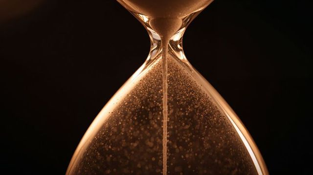 Macro amber hourglass flowing sand through narrow neck closeup with glowing rim and bokeh