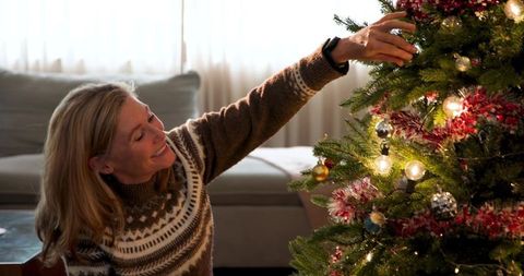 Senior woman decorating christmas tree in cozy living room