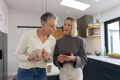 Two women sharing coffee and smartphone at modern minimalist kitchen island