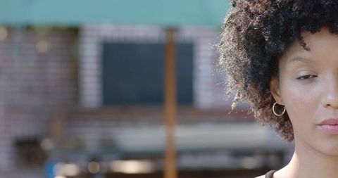 Contemplative sunlit african woman looking down half-face portrait candid with copy space