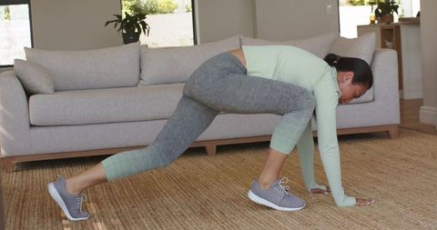 Asian woman performing low lunge stretch during home workout in bright living room