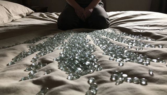 Kneeling man clasping hands over bed with glass gems radiating across duvet
