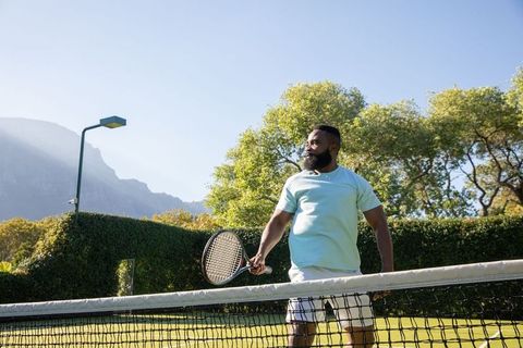 Athletic man standing at grass tennis court beside net on sunny day