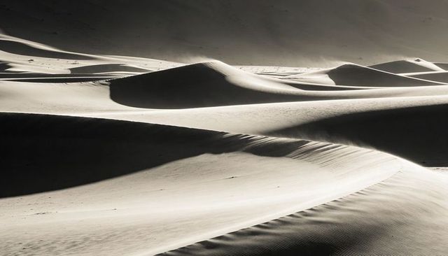Monochrome sand dunes sculpting smooth ridges and wind ripples under dramatic light