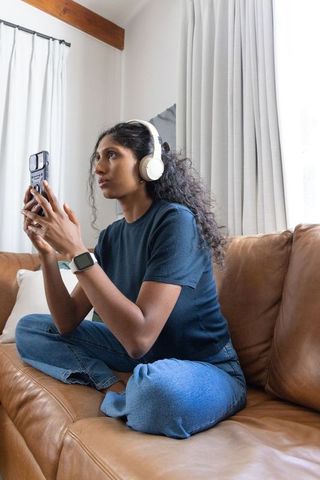 African american woman wearing headphones and using smartphone on leather sofa