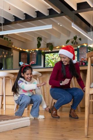 Asian mother and daughter laughing and playing in festive kitchen with santa hat and antlers