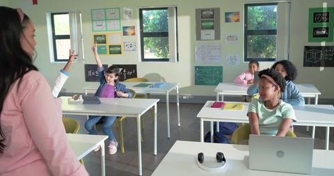 Diverse students listening to teacher in modern classroom with laptops and tablets