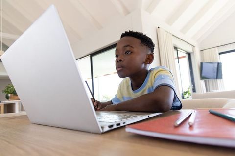 African american boy studying on laptop at home doing remote learning and homework
