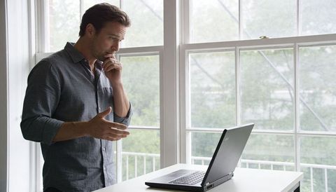 Thoughtful man gesturing during remote video call at laptop by bright window, home office