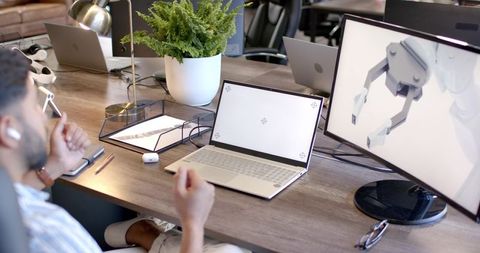 Indian man gesturing at robotic gripper on monitor while collaborating at modern workspace