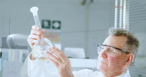 Senior chemist inspecting round-bottom flask in modern lab wearing protective goggles