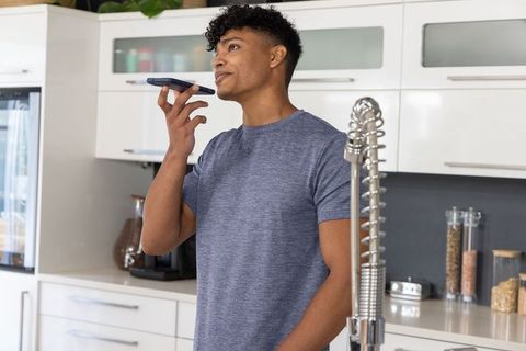 Young african american man using voice assistant in modern kitchen for smart home control