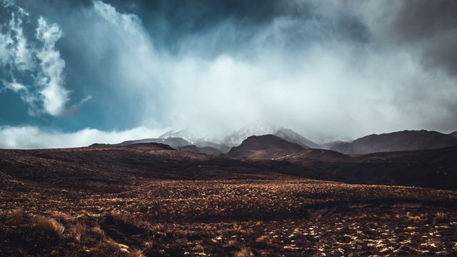 Expansive view of mountainous terrain under stormy skies creating a dramatic effect. Useful for nature-related publications, travel blogs, or thematic backdrops for multimedia projects.