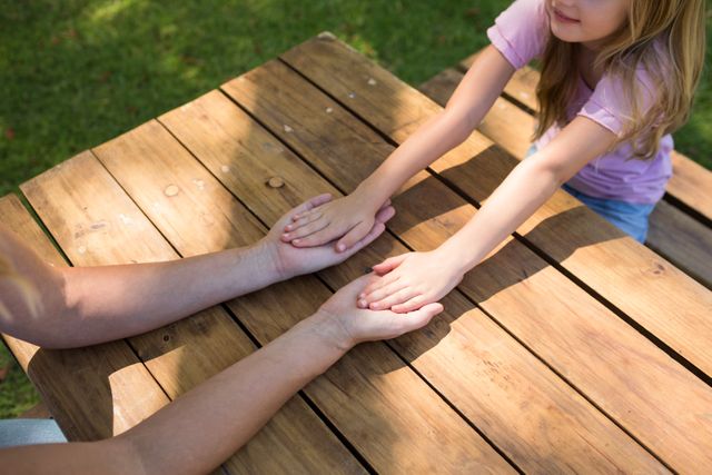 Mother and daughter holding hands on picnic table in park