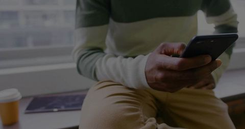 Man relaxing on window ledge checking smartphone