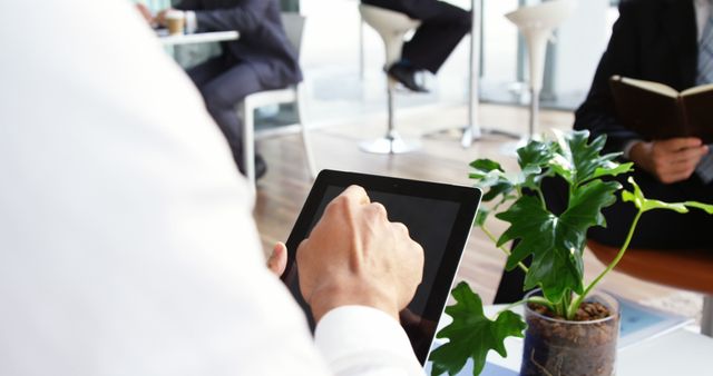 Business professional using a tablet in a modern office environment. Plant on the desk adds a touch of greenery. Ideal for use in articles, blogs, and websites focusing on technology in the workplace, productivity, and modern office settings.