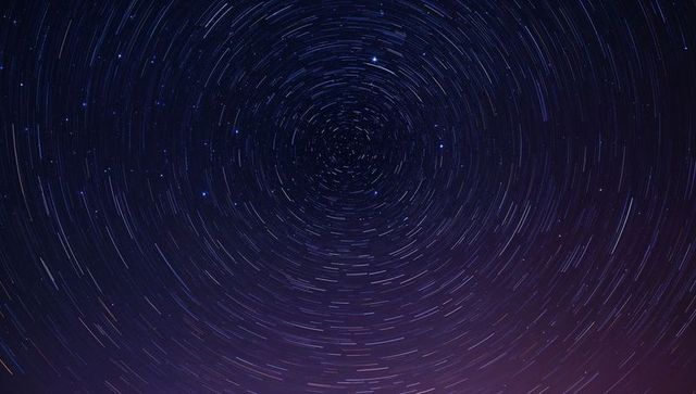 Rotating star trails circling celestial pole over purple night horizon