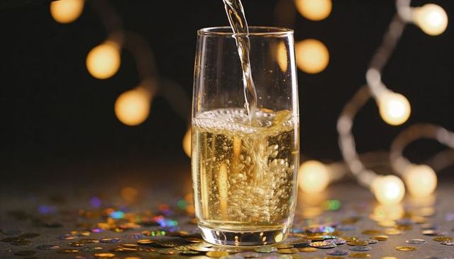 Pouring sparkling drink into tumbler with golden confetti and warm bokeh lights