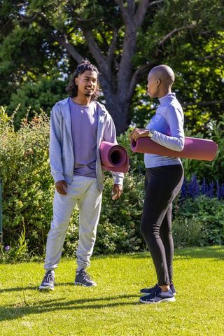 Two african american friends holding yoga mats chatting in park before outdoor workout
