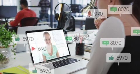 Remote team member watching live video call on laptop with social notifications in open office
