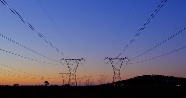 Electricity pylons stretch across a twilight sky, showcasing infrastructure. Power lines form a silhouette against the fading light, emphasizing energy distribution.