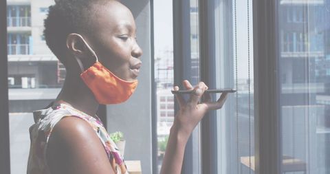 Businesswoman Using Smartphone While Wearing Face Mask Near Window