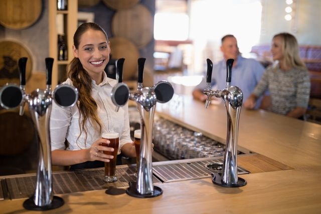 Portrait of female bartender holding glass of beer at bar counter