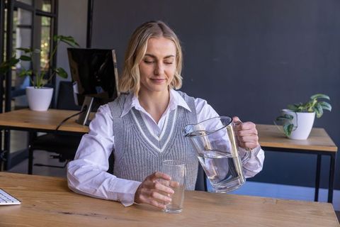 Professional woman pouring water in modern office with plants