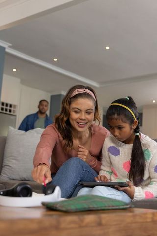 Multicultural mother guiding daughter using tablet on cozy living room sofa with father